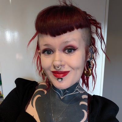 Person with tattoos and piercings wearing a black top against a neutral background